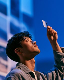 A young man holding a small card up to the light, against deep blue.